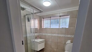 Een badkamer met douche, toilet en wastafel.
