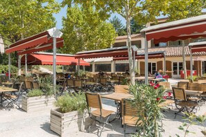 An outdoor cafe with wooden tables and chairs, covered by red awnings, and surrounded by planters. - Spacious Duplex Retreat for 8 (Grospierres)