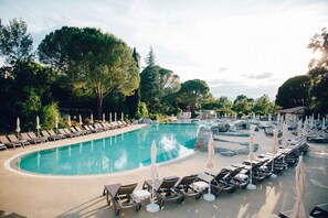Un espace piscine agrémenté de chaises longues et de parasols, entouré d’arbres.
