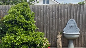 A garden with a wooden fence, a green bush, a statue, and a stone fountain. - Luxury annex, close to Newquay beaches, town, and amenities! Peaceful spot! (Newquay)