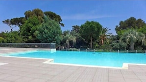 A swimming pool with a tiled deck, surrounded by trees and a clear sky. - Apartment with pool and garden in Saint Aygulf (Fréjus)