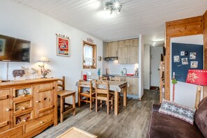 Ein gemütliches Zimmer mit einem Holztisch, Stühlen, einer Couch, einem Fernseher und einer Küchenzeile mit Holzschränken.