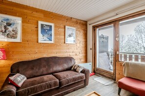 Ein gemütliches Zimmer mit einem braunen Sofa, Holzwänden und einem großen Fenster mit Blick auf eine verschneite Landschaft.