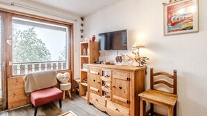 A cozy room with a wooden bench, a TV, a wooden cabinet, and a window with a view of trees. - Le Nid de Châtel - Joli studio pour 4 avec balcon (Châtel)