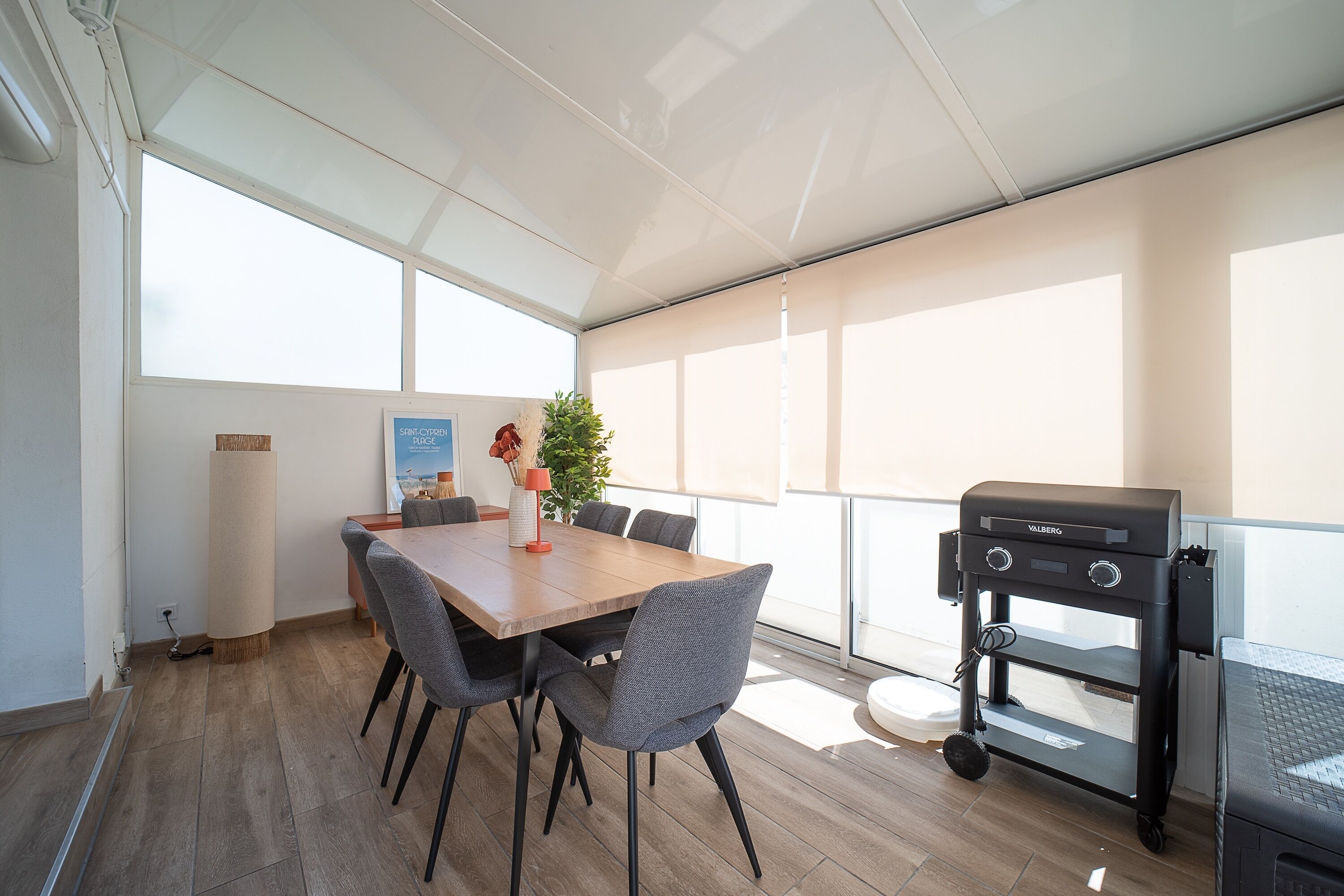Un espace repas avec une table et des chaises en bois, un barbecue et une plante.