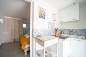 A modern kitchen with white cabinets, a small island, and a tiled backsplash. - Bohème Bleue - 500m de la Plage (Saint-Cyprien)