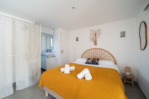 A bedroom with a bed, a bathroom, a wooden headboard, a small side table, and a wall-mounted mirror. - Bohème Bleue - 500m de la Plage (Saint-Cyprien)