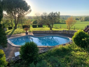A swimming pool with a wooden deck, surrounded by lush greenery and trees. - Villa Douceur - Avec piscine privée et sauna (Condom)
