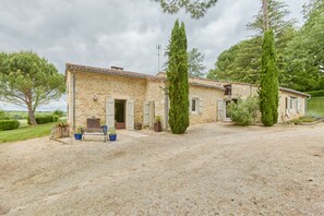 A stone house with a gravel driveway, two tall cypress trees, and a bench with potted plants. - Villa Douceur - Avec piscine privée et sauna (Condom)
