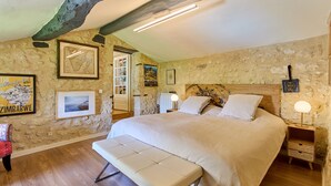 Un dormitorio con una cama grande, piso de madera, paredes de piedra y cuadros enmarcados.