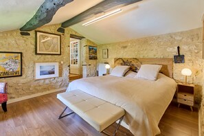 A bedroom with a large bed, wooden floor, stone walls, and framed pictures. - Villa Douceur - Avec piscine privée et sauna (Condom)
