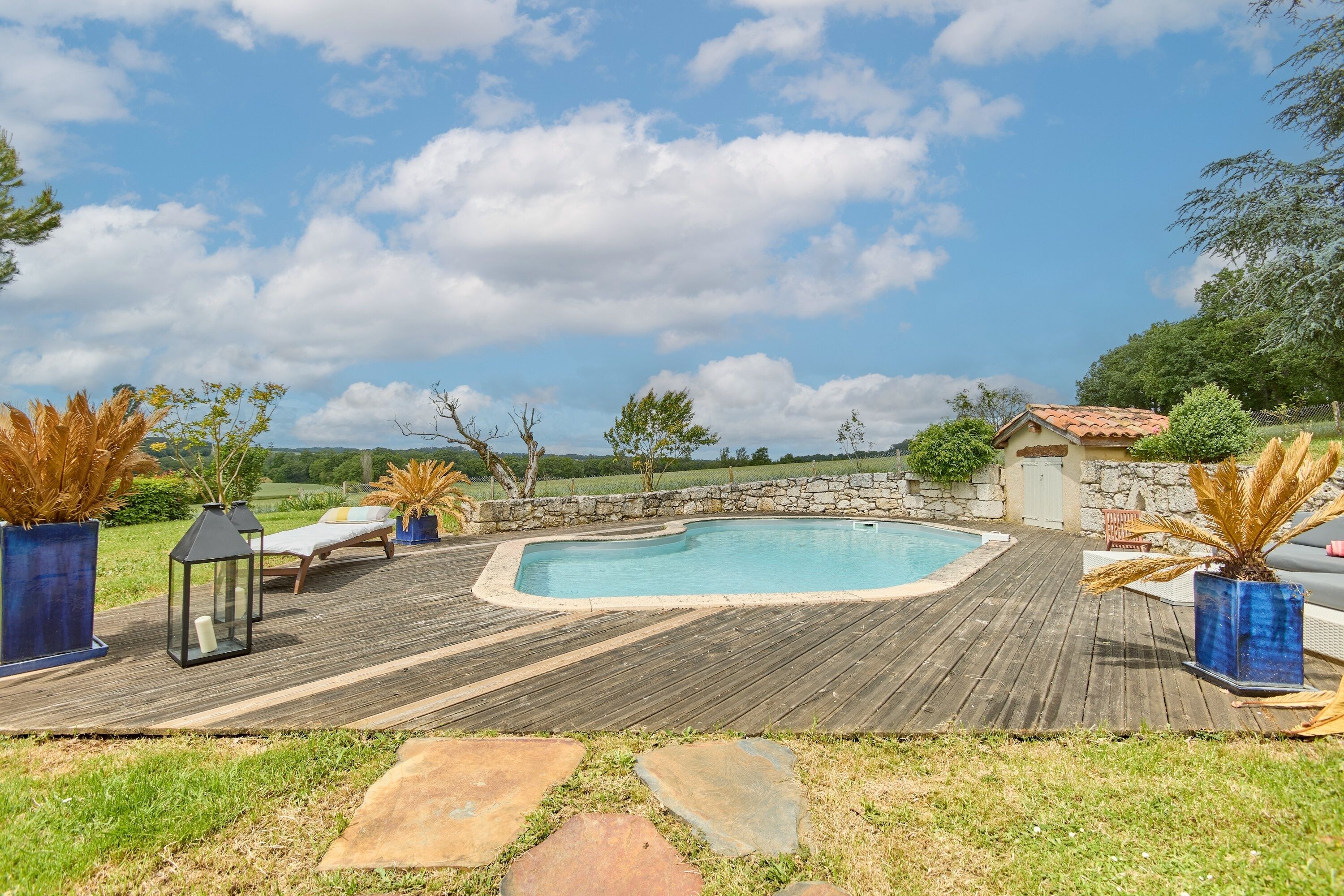 A wooden deck with a pool, lounge chairs, and potted plants.