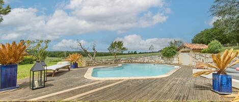 A wooden deck with a pool, lounge chairs, and potted plants.