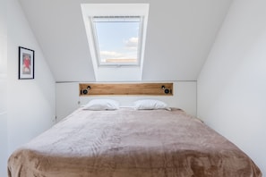 Una camera da letto con soffitto spiovente, un lucernario, una testiera in legno e un letto con cuscini bianchi.