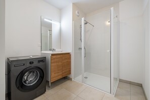 Ein modernes Badezimmer mit Waschmaschine, Waschbecken und einer Duschkabine.
