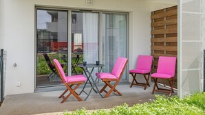 Ein Balkon mit zwei Tischen und vier Stühlen, einer Glastür und einer Holzwand.