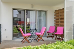 Ein Balkon mit zwei Tischen und vier Stühlen, einer Glastür und einer Holzwand.