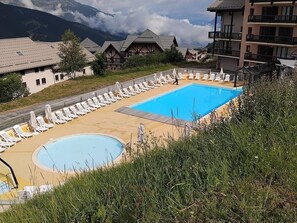 A pool area with lounge chairs, a smaller circular pool, and buildings with balconies in the background. - Le Thabor Caribou - À 650 m des pistes (Valmeinier)