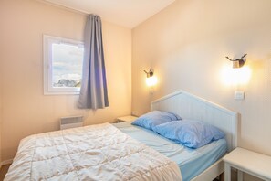 A bedroom with a bed, a nightstand, a wall-mounted light fixture, and a window with a view of mountains. - Le Thabor Caribou - À 650 m des pistes (Valmeinier)