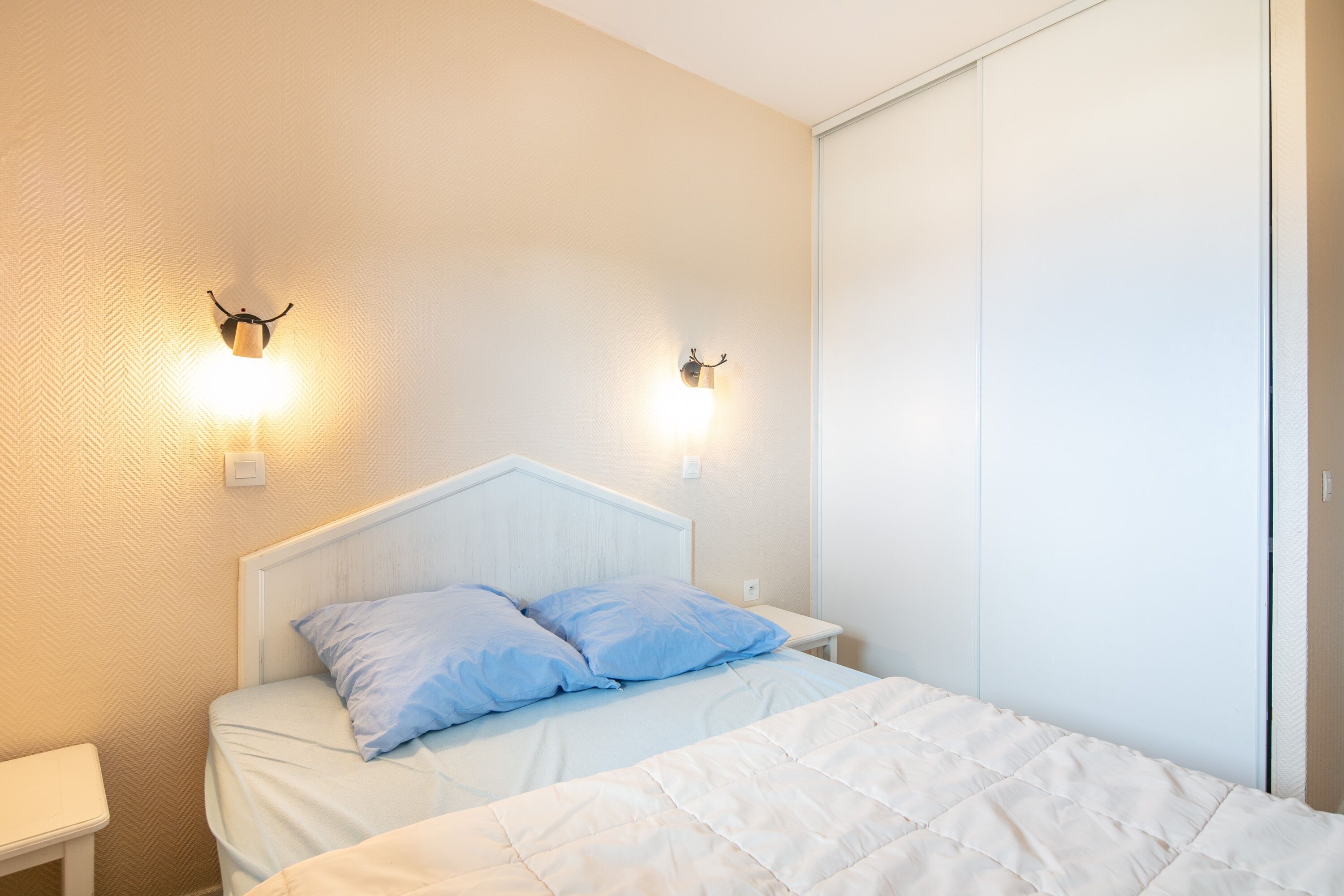 A bedroom with a bed, two wall-mounted light fixtures, a bedside table, and a wardrobe.