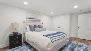 A bedroom with a bed, bedside table, lamp, and a painting on the wall.