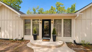 Une maison de plain-pied avec un porche à l’avant, une porte noire et deux plantes en pot.