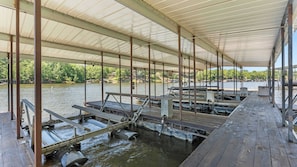 Een overdekte steiger met houten banken en tafels, omringd door water.