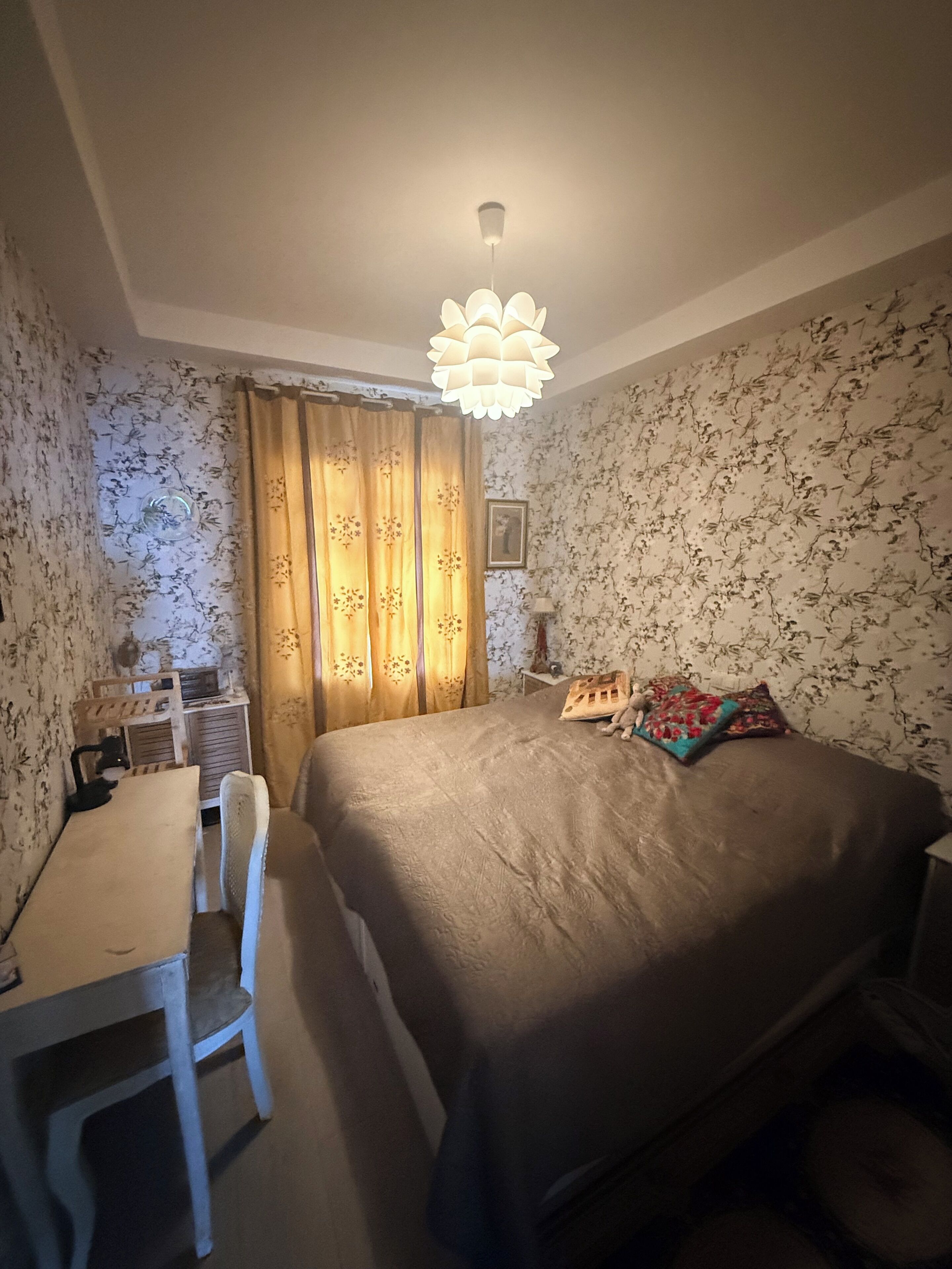 Une chambre à coucher comprenant un lit, un bureau, une chaise, une table de chevet et une lampe fixée au mur.
