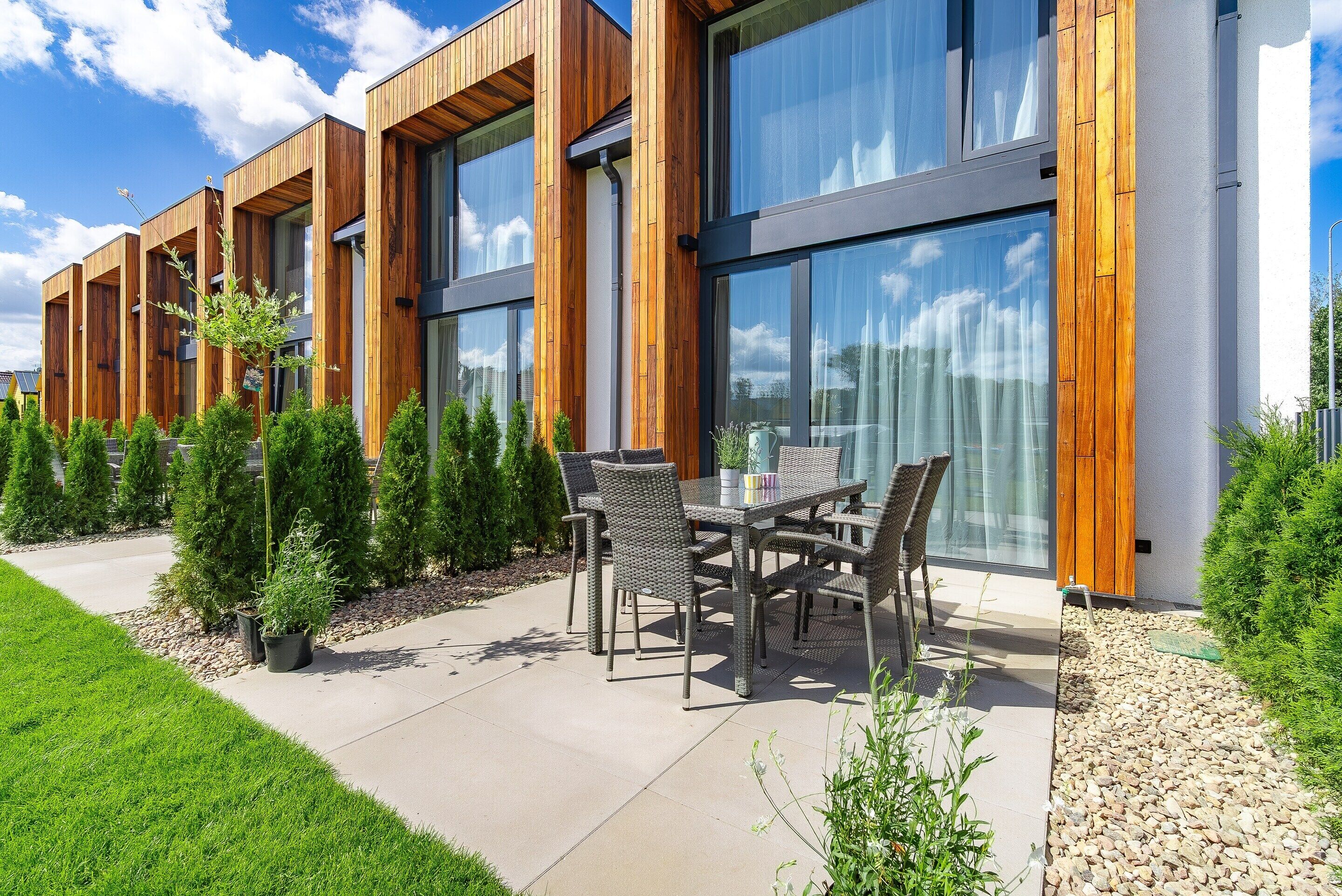 Een modern gebouw met grote ramen, een terras met tuinmeubilair en een verzorgde tuin.