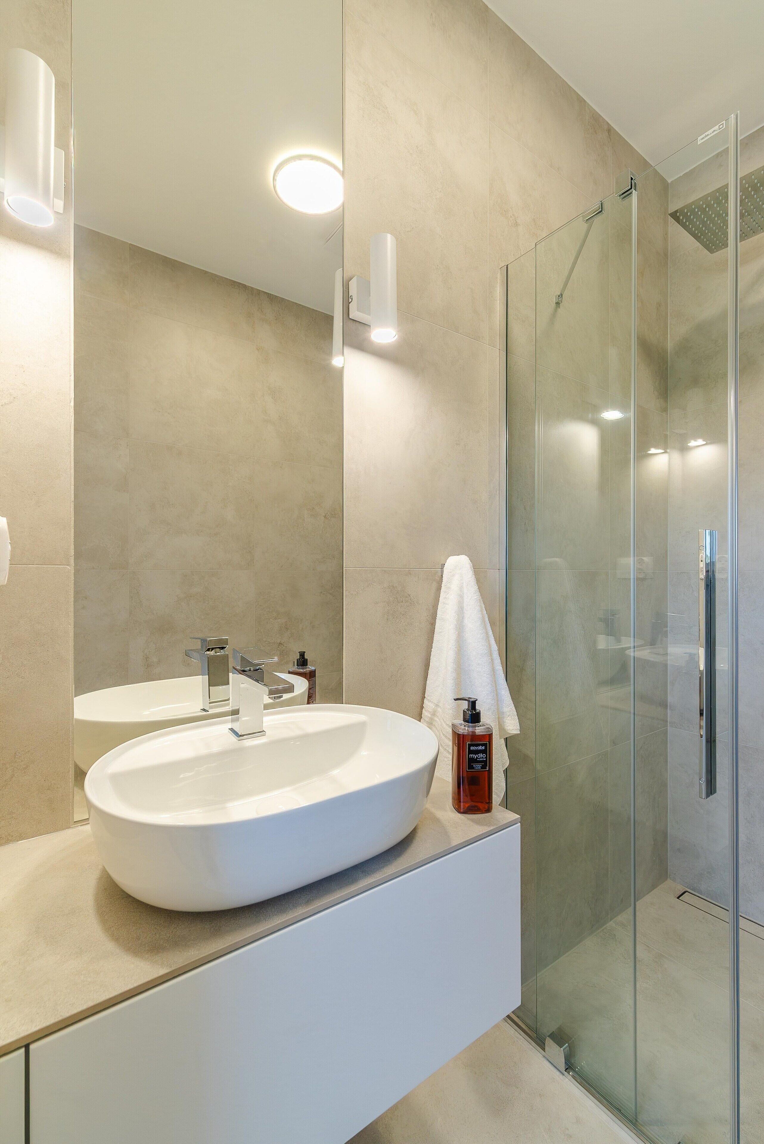 A modern bathroom with a large white sink, a glass shower enclosure, and a mirror.