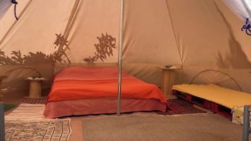 A tent with a bed, a table, and a hanging item.