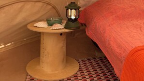 Interior de una carpa con un farol, una mesita con conchas marinas y una manta estampada.