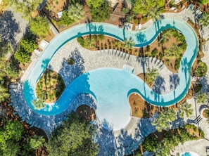 Eine Vogelperspektive auf einen gewundenen Pool, umgeben von Palmen und Liegestühlen.