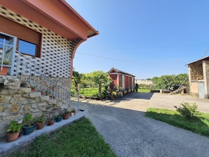 Ein Haus aus Stein mit einer Metalltreppe, im Hintergrund ein Gebäude aus rotem Backstein und eine Auffahrt mit Kies.