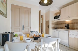 Une cuisine moderne avec des meubles blancs, un grille-pain, une machine à café et un coin repas avec une table mise pour le petit-déjeuner.