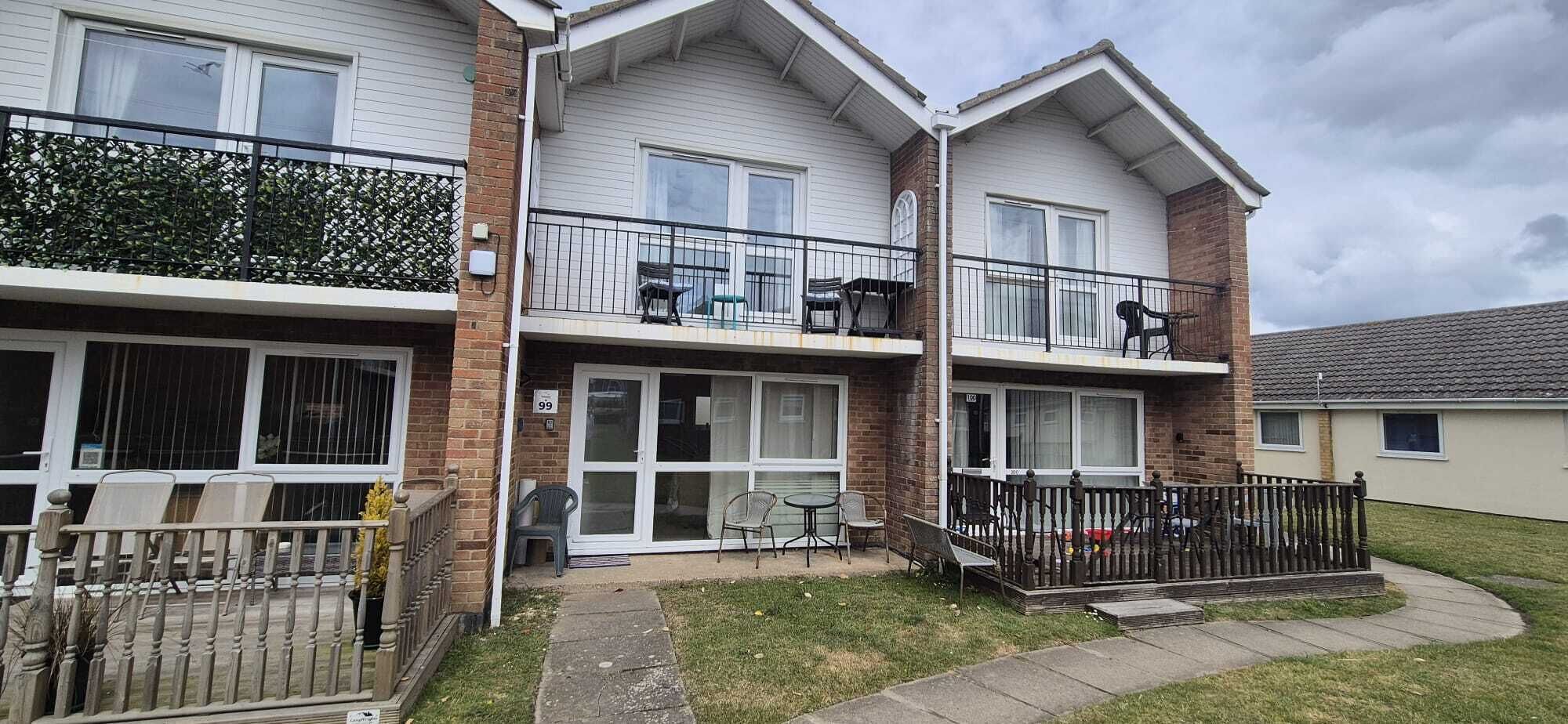 A two-story residential building with a balcony, a patio with outdoor furniture, and a gated entrance.. Beach holiday home pet friendly Great for relaxing