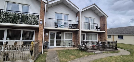 A two-story residential building with a balcony, a patio with outdoor furniture, and a gated entrance.. Beach holiday home pet friendly Great for relaxing