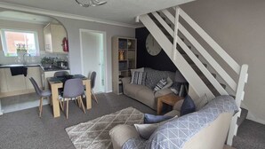 Un espace de vie compact comprenant un coin repas, un canapé, un escalier et une cuisine.