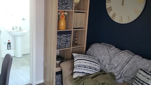 Un salon avec un canapé, une bibliothèque, une horloge et une vue sur une salle de bain.