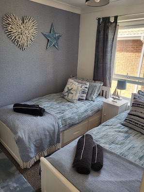 Un dormitorio con dos camas, decoración de pared con estrellas, decoración de pared con estrellas de mar, una ventana con cortinas y una mesita de noche con lámpara.
