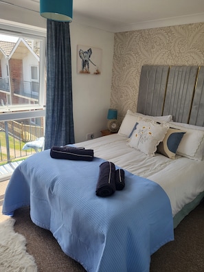 A bedroom with a bed, a window, a curtain, a wall clock, and a decorative wall piece. - Beach holiday home pet friendly Great for relaxing (Corton)