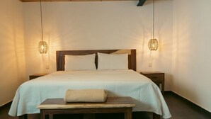 Un dormitorio ordenado con cama, mesitas de noche, un banco y lámparas colgantes.