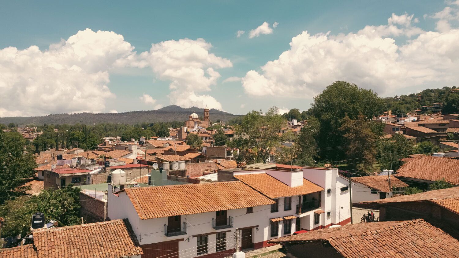 A town with terracotta-roofed buildings, a prominent church with a dome, and a hill in the background.