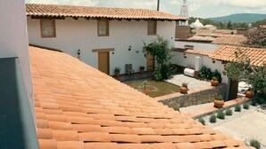 Un patio con techos de tejas de terracota, un edificio blanco con puerta de madera y una iglesia blanca con campanario al fondo.