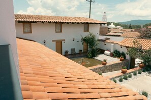 Un patio con techos de tejas de terracota, un edificio blanco con puerta de madera y una iglesia blanca con campanario al fondo.