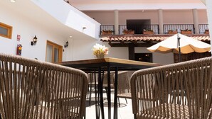 Un amplio patio al aire libre con mobiliario de mimbre, una mesa central y un balcón con plantas en macetas.