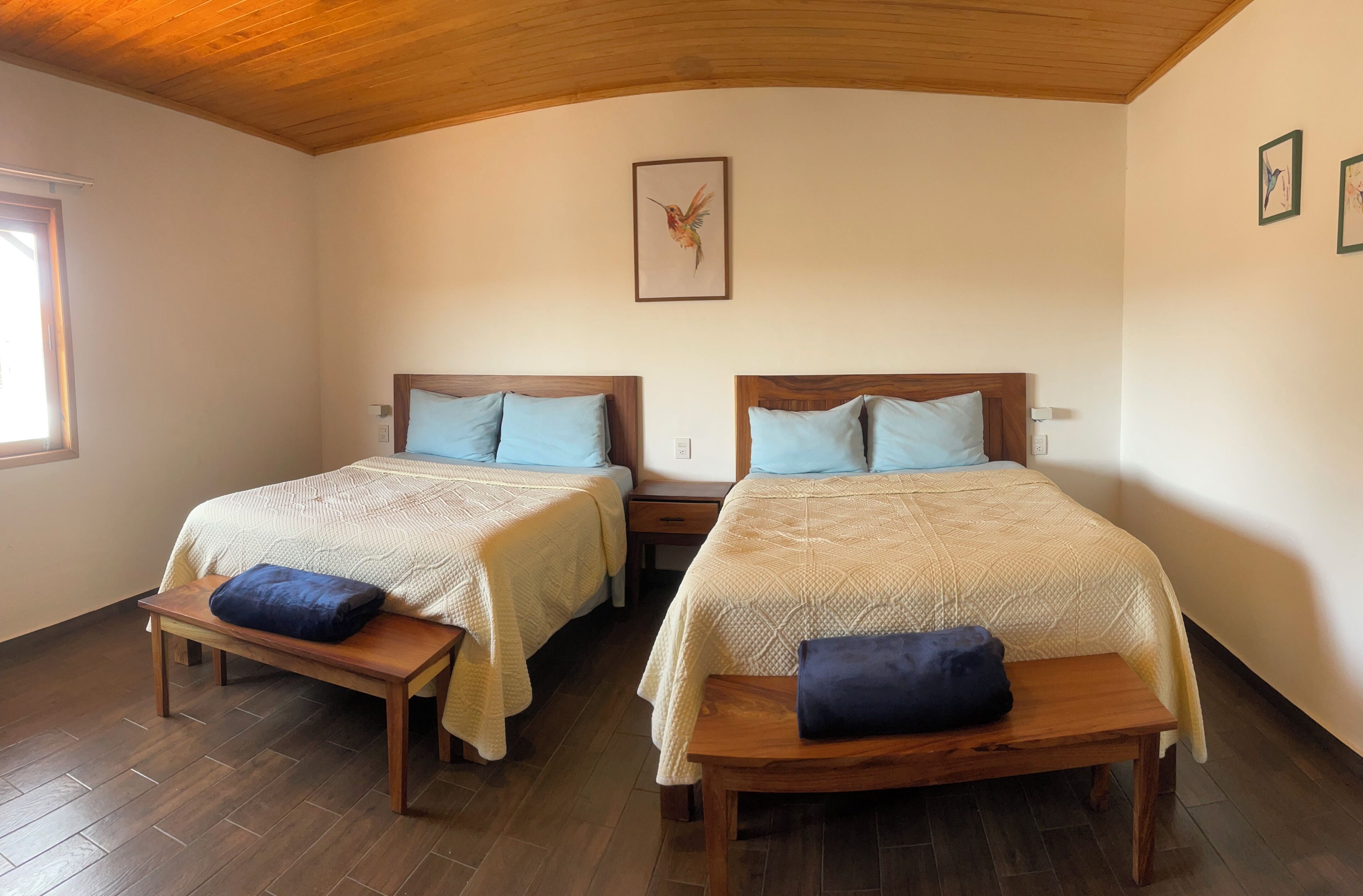 A room with two beds, wooden benches, a wooden ceiling, and a framed picture on the wall.