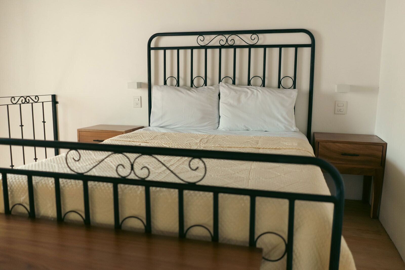 A single bed with a metal frame, two bedside tables, and a plain wall.