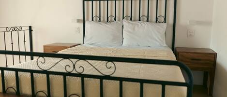 A single bed with a metal frame, two bedside tables, and a plain wall.