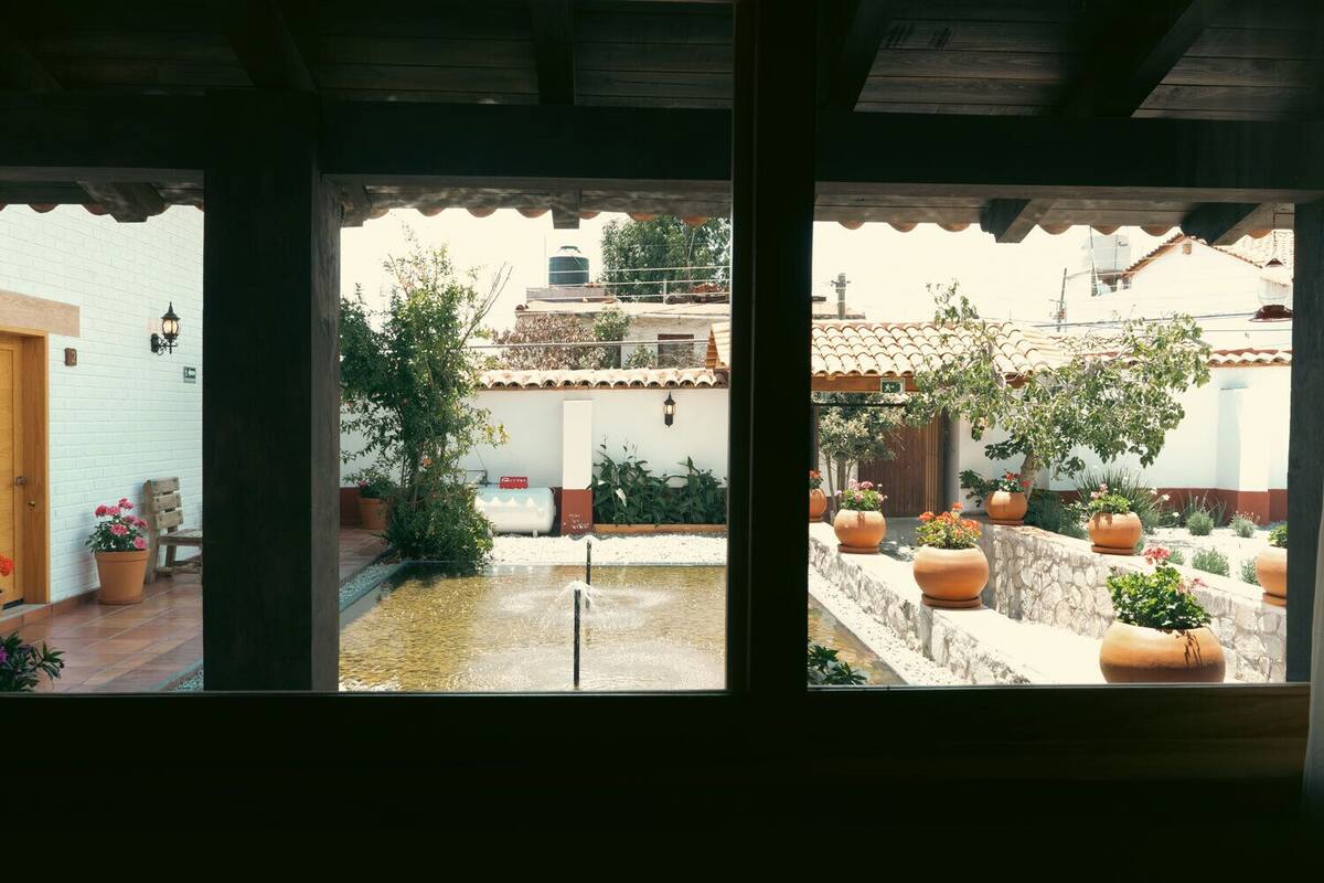 Un patio con fuente, plantas en macetas y vista a un edificio con techo de tejas.